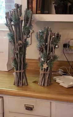 two vases made out of branches and pine cones on top of a wooden counter