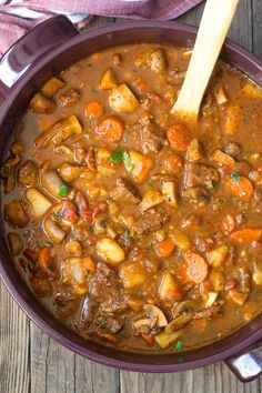 a purple bowl filled with meat and vegetable soup on top of a wooden table next to a spoon