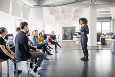 a woman standing in front of a group of people while holding a clipboard and talking to them