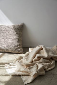 a blanket and pillows on the floor in front of a wall with sunlight coming through it