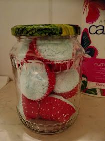 a glass jar filled with red and white knitted snowballs next to a carton of candy