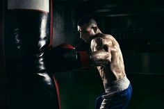 a shirtless man wearing boxing gloves is in the dark with his hand on a punching bag