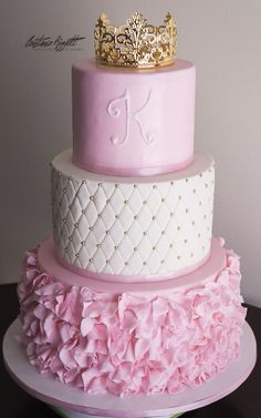 a three tiered cake with pink ruffles and a gold crown on top