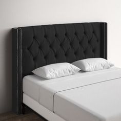 a black headboard with white pillows on top of it and a wooden floor in the background