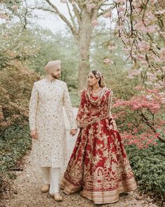 two people standing next to each other in front of trees and bushes with pink flowers