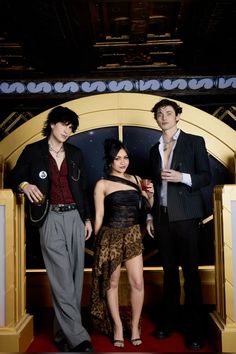 two men and a woman standing in front of a stage with a red carpet on the floor