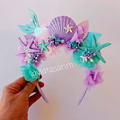 a hand holding a purple and green headband with seashells, stars and pearls