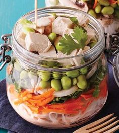 two mason jars filled with food on top of a blue table next to a wooden spoon