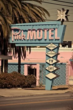 a motel sign in front of a palm tree on the side of the road with pink buildings behind it