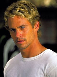 a man with blonde hair wearing a white t - shirt and looking at the camera