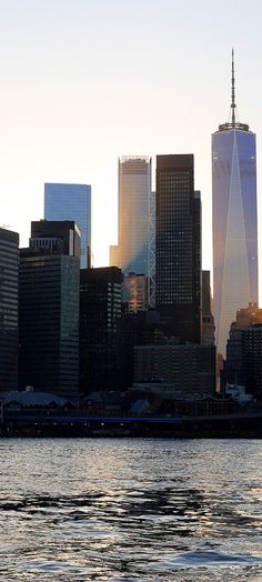 the skyline of new york city is seen from across the water at sunset, with one world trade center in the foreground