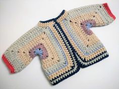 a crocheted sweater sitting on top of a white table next to a blue and red object