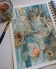 an art journal is open on a table next to a paintbrush and some gold flakes