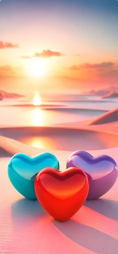 three heart shaped bowls sitting on top of a beach near the ocean in front of a sunset