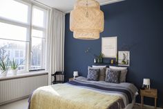 a bed room with a neatly made bed next to a window and a lamp hanging from the ceiling