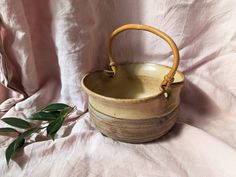 a wooden basket sitting on top of a white cloth covered bed next to a plant