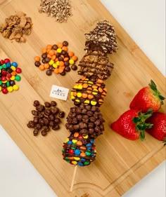 a wooden cutting board topped with lots of candy and candies next to strawberries