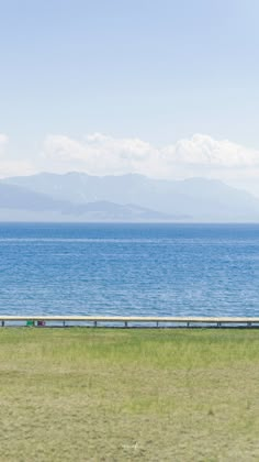 two people riding horses on the side of a road by the ocean with mountains in the background