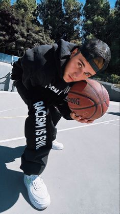 a young man holding a basketball on top of a basketball court with trees in the background