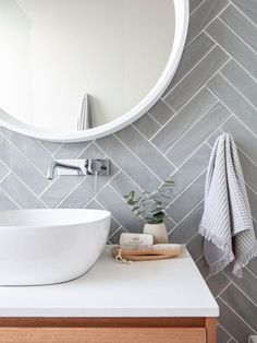 a white sink sitting under a round mirror next to a wooden cabinet with towels on it