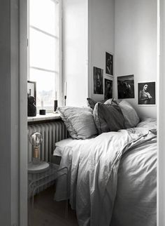 black and white photograph of a bed in a small room with pictures on the wall