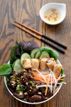 a bowl filled with meat and veggies next to chopsticks on a wooden table