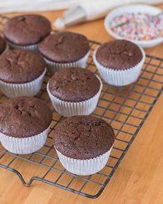 twelve chocolate cupcakes on a cooling rack with sprinkles next to them