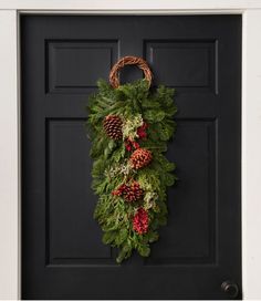 a wreath hanging on the front door decorated with pine cones and evergreen leaves, red berries and green foliage