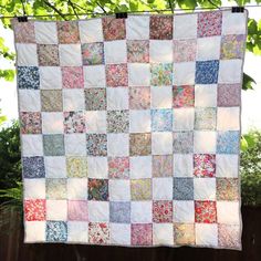 a quilt hanging from a clothes line with trees in the background