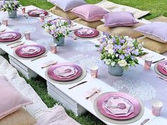 a table set up with pink and purple plates, napkins and flowers in vases