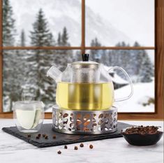 a glass tea pot with white wine in front of a snowy mountain view and window