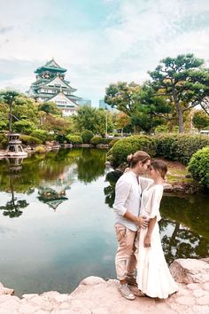 a man and woman standing next to each other in front of a pond