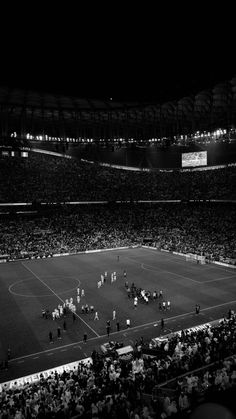 a stadium filled with lots of people standing on top of a soccer field at night