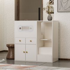 a white cabinet sitting on top of a tiled floor next to a vase with flowers