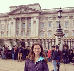 a woman standing in front of a large building with lots of people around it on the sidewalk