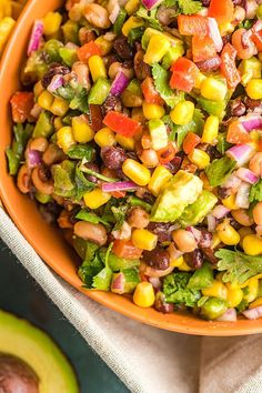 an orange bowl filled with corn salad next to sliced avocado and cilantro