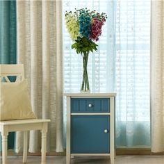 a vase with flowers sitting on top of a blue cabinet next to a white chair