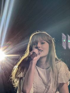 a woman singing into a microphone while standing in front of a stage with bright lights