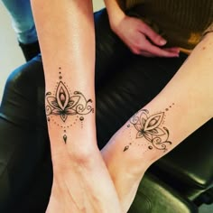 two people with matching tattoos on their legs sitting down together, one is holding the other's hand