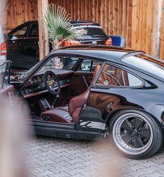 an old black car parked in front of a wooden building with its door open and the driver's seat up