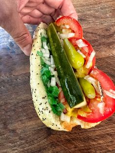 a person holding a sandwich with tomatoes, peppers and cucumbers