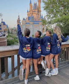 three girls in mickey mouse sweatshirts standing on a bridge with their arms up to the sky