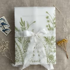 a gift wrapped in white paper and tied with a ribbon, surrounded by dried flowers