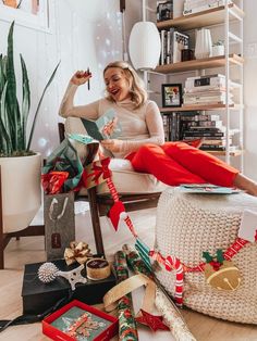 a woman sitting on a chair surrounded by christmas decorations and presents, with her feet up in the air