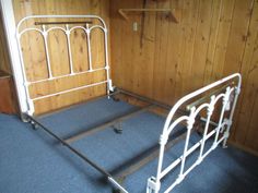 a white metal bed frame sitting in a bedroom next to a wall with wood paneling