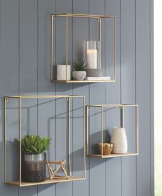 two gold metal wall shelves with plants and candles on them, against a blue painted wall