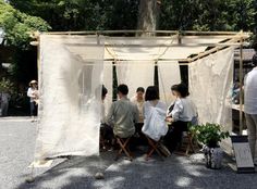 some people are sitting in chairs under a white tent with curtains on it and plants