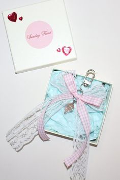 an open gift box with a pink ribbon and keychain attached to it, sitting on a white surface