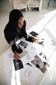 a woman is sitting at a table with many papers on it and looking through the pages