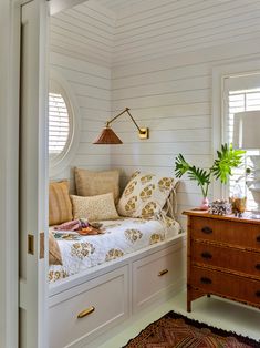 a bedroom with white walls and wooden furniture in the foreground is a small window